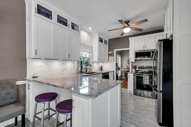 kitchen featuring light stone counters, kitchen peninsula, stainless steel appliances, tasteful backsplash, and white cabinets