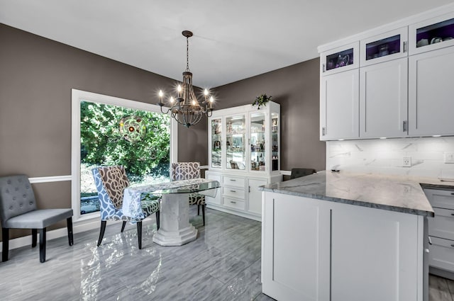 kitchen with a chandelier, decorative backsplash, white cabinets, stone countertops, and decorative light fixtures