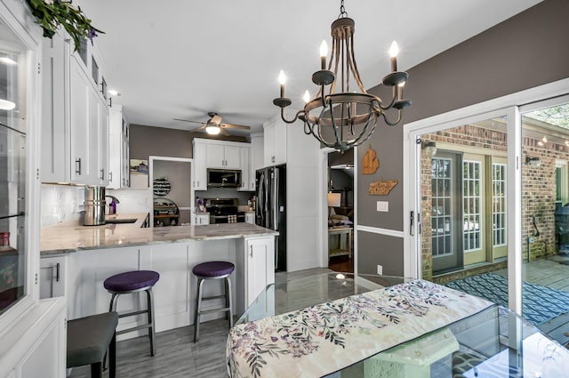 kitchen with kitchen peninsula, decorative backsplash, white cabinetry, ceiling fan with notable chandelier, and appliances with stainless steel finishes