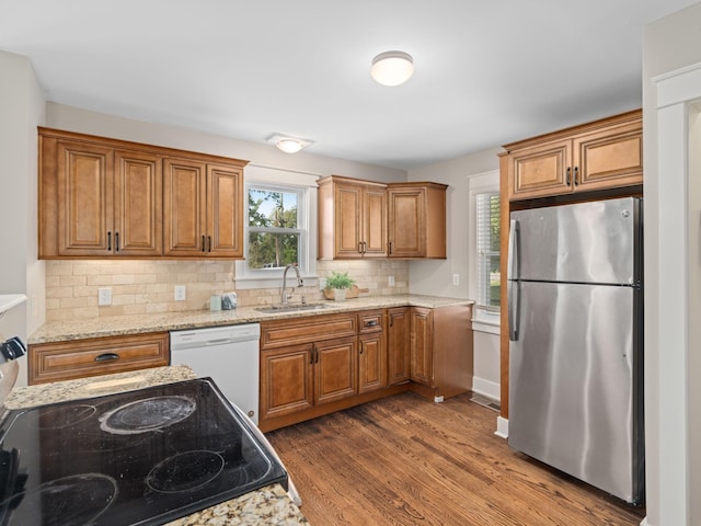 kitchen featuring stainless steel appliances, sink, light stone counters, backsplash, and dark hardwood / wood-style flooring