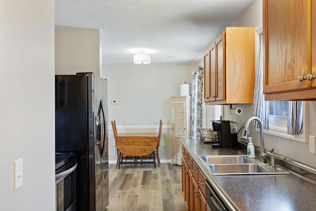 kitchen featuring sink, light wood-type flooring, appliances with stainless steel finishes, and a textured ceiling