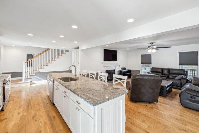 kitchen with sink, white cabinetry, light hardwood / wood-style flooring, light stone countertops, and a kitchen island with sink