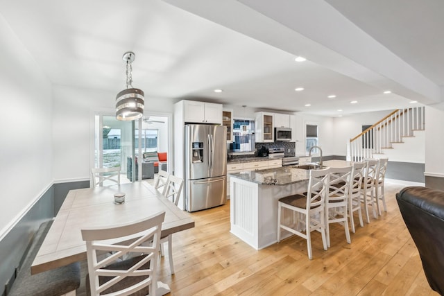 kitchen with decorative light fixtures, stainless steel appliances, white cabinets, dark stone countertops, and sink