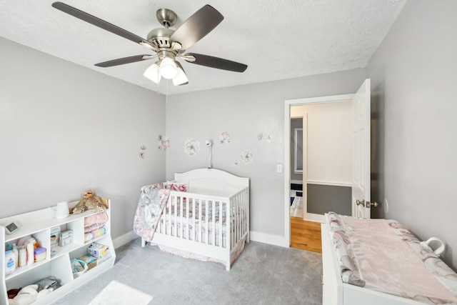 carpeted bedroom featuring a nursery area, a textured ceiling, and ceiling fan