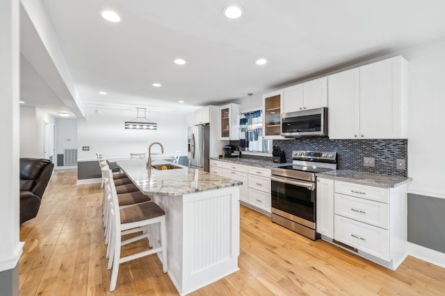 kitchen featuring a breakfast bar, stainless steel appliances, an island with sink, and white cabinetry