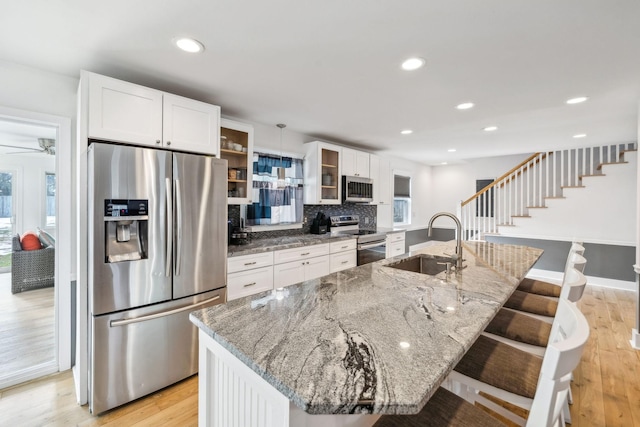 kitchen with a center island with sink, stainless steel appliances, a breakfast bar, light stone counters, and sink