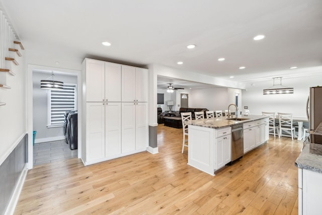 kitchen with white cabinets, pendant lighting, light stone counters, and a center island with sink