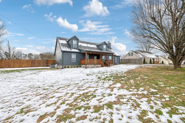 snow covered back of property with central AC and covered porch