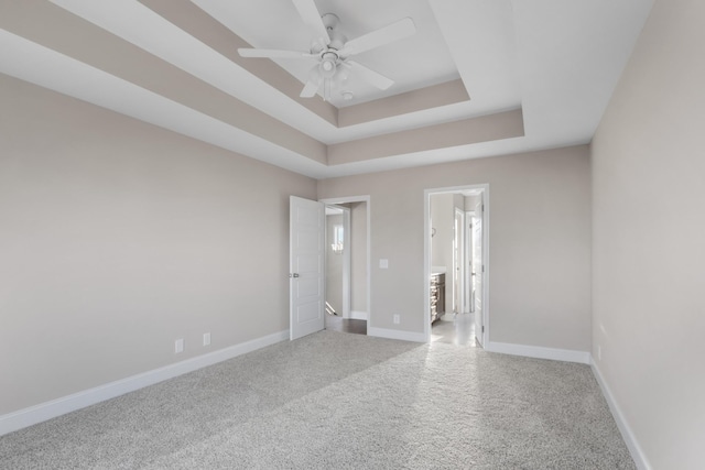 carpeted empty room with ceiling fan and a raised ceiling