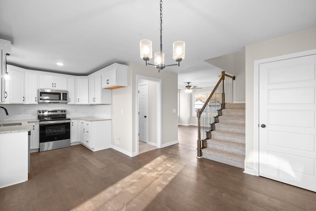 kitchen featuring appliances with stainless steel finishes, pendant lighting, ceiling fan with notable chandelier, white cabinets, and sink