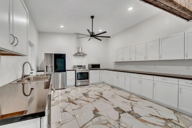 kitchen featuring wall chimney exhaust hood, white cabinetry, appliances with stainless steel finishes, ceiling fan, and sink