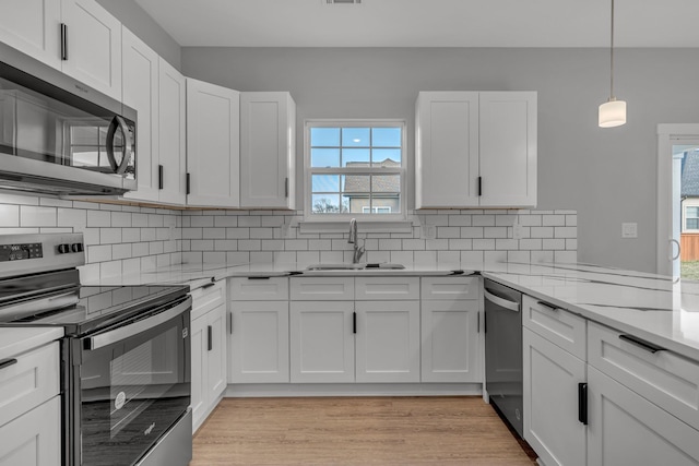 kitchen featuring light stone countertops, pendant lighting, white cabinetry, stainless steel appliances, and sink