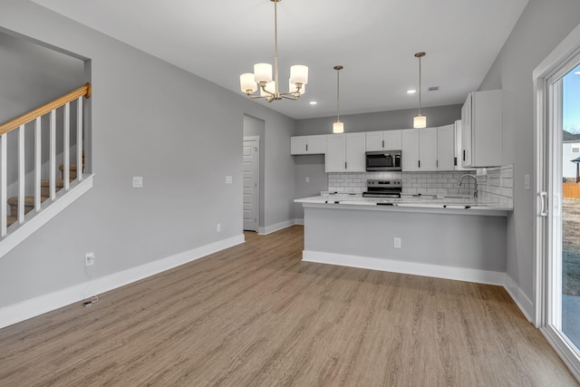 kitchen with white cabinetry, kitchen peninsula, appliances with stainless steel finishes, decorative backsplash, and a notable chandelier