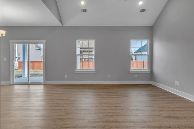 unfurnished room featuring a healthy amount of sunlight, vaulted ceiling, an inviting chandelier, and wood-type flooring