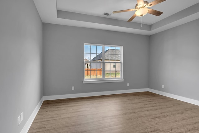 empty room with ceiling fan, light hardwood / wood-style floors, and a raised ceiling