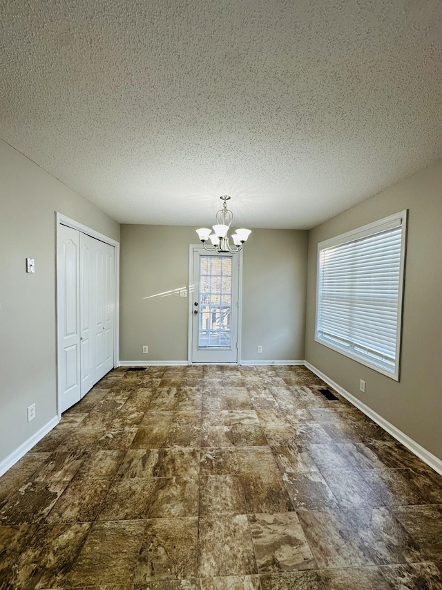 spare room with a textured ceiling, a chandelier, and a healthy amount of sunlight