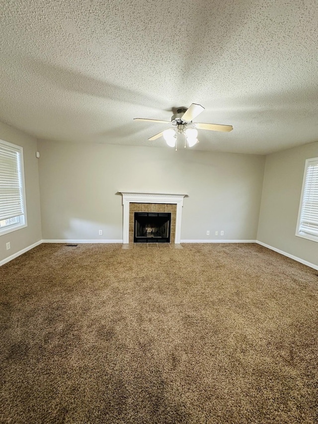 unfurnished living room with carpet flooring, ceiling fan, a tile fireplace, and a wealth of natural light