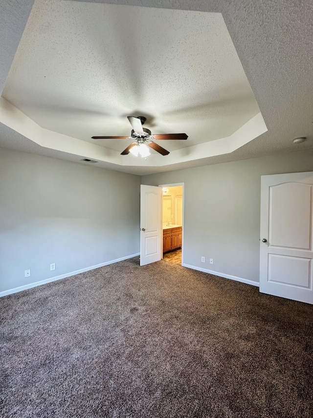 unfurnished bedroom featuring carpet, ceiling fan, a tray ceiling, a textured ceiling, and ensuite bathroom