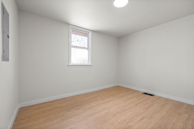 spare room featuring electric panel and light hardwood / wood-style flooring