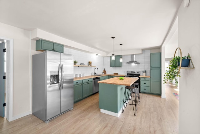 kitchen featuring appliances with stainless steel finishes, a breakfast bar, wall chimney exhaust hood, sink, and butcher block counters