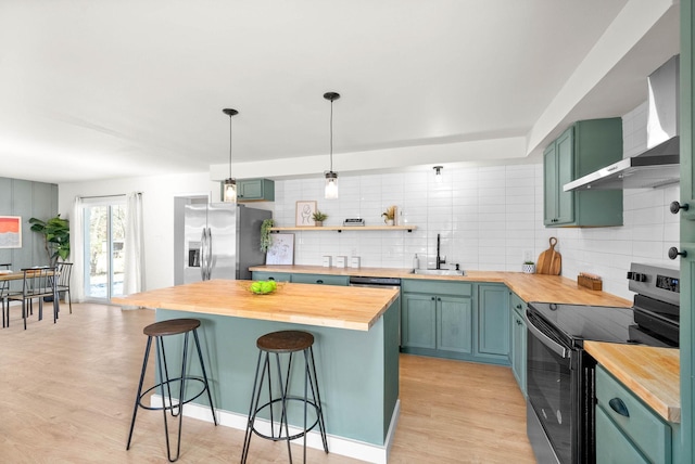 kitchen featuring hanging light fixtures, stainless steel appliances, wall chimney range hood, wood counters, and a breakfast bar area