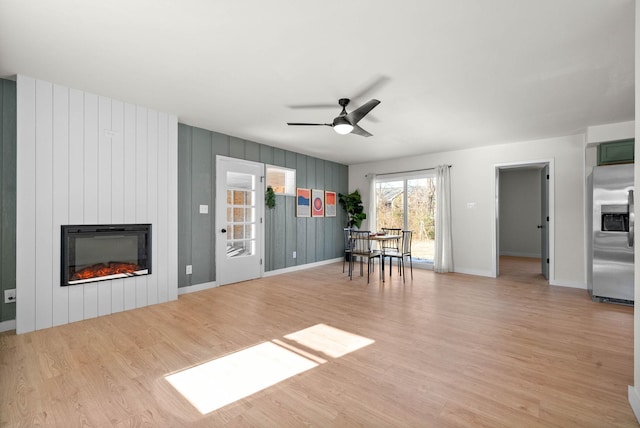 unfurnished living room featuring ceiling fan, light wood-type flooring, wooden walls, and a fireplace