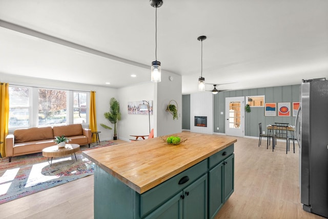 kitchen featuring stainless steel refrigerator, hanging light fixtures, ceiling fan, a fireplace, and a kitchen island