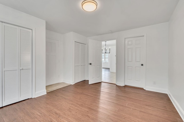 unfurnished bedroom featuring multiple closets, an inviting chandelier, and light hardwood / wood-style flooring