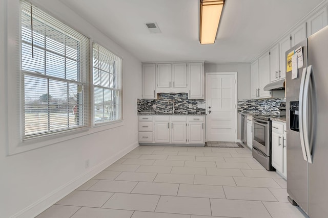 kitchen with light tile patterned floors, appliances with stainless steel finishes, white cabinets, light stone counters, and sink