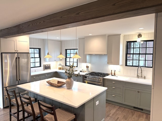 kitchen with sink, hanging light fixtures, premium appliances, a kitchen breakfast bar, and light stone countertops