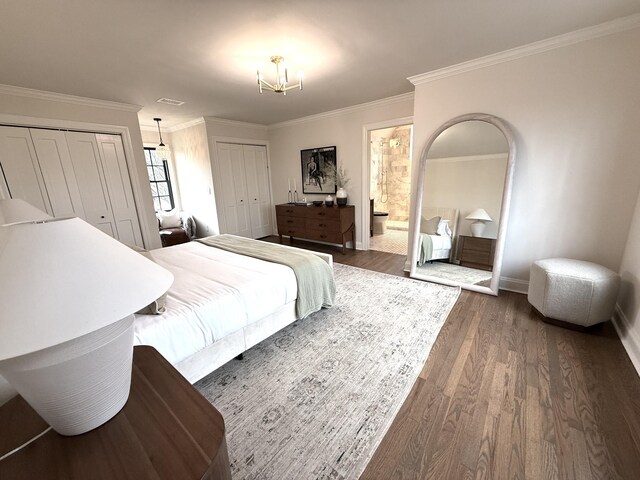 bedroom featuring dark wood-type flooring, ornamental molding, a chandelier, and multiple closets