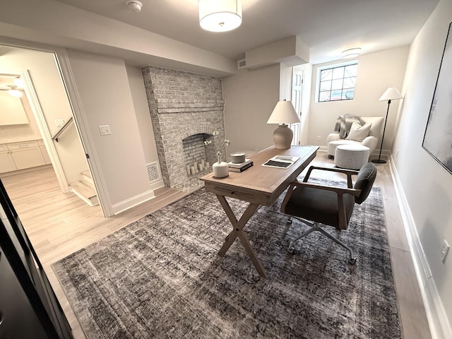 office area with a brick fireplace and light hardwood / wood-style floors