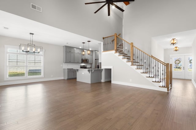 unfurnished living room with plenty of natural light, dark wood-type flooring, ceiling fan with notable chandelier, and high vaulted ceiling