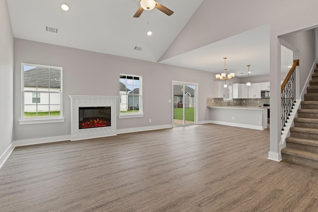 unfurnished living room with ceiling fan with notable chandelier, high vaulted ceiling, and wood-type flooring