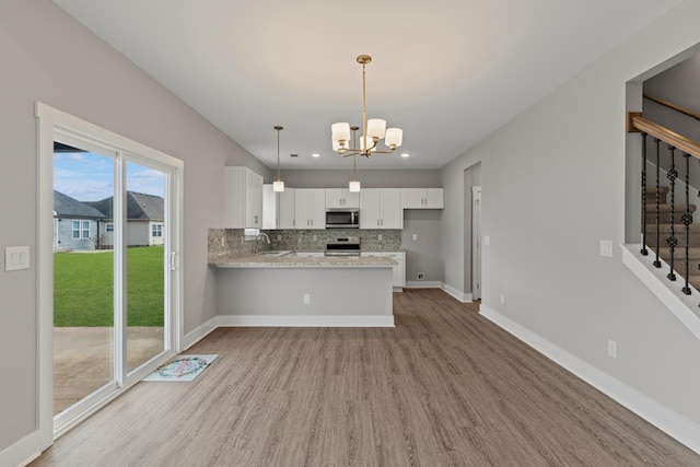 kitchen with appliances with stainless steel finishes, kitchen peninsula, white cabinets, backsplash, and sink