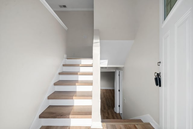 staircase with wood-type flooring and crown molding