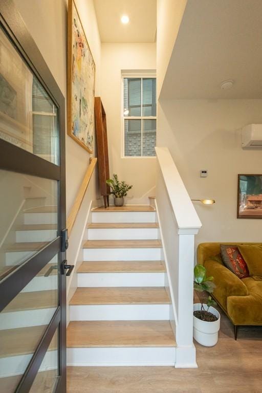 stairway with a wall unit AC and hardwood / wood-style floors