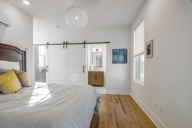 bedroom featuring an AC wall unit, ensuite bath, light wood-type flooring, and a barn door