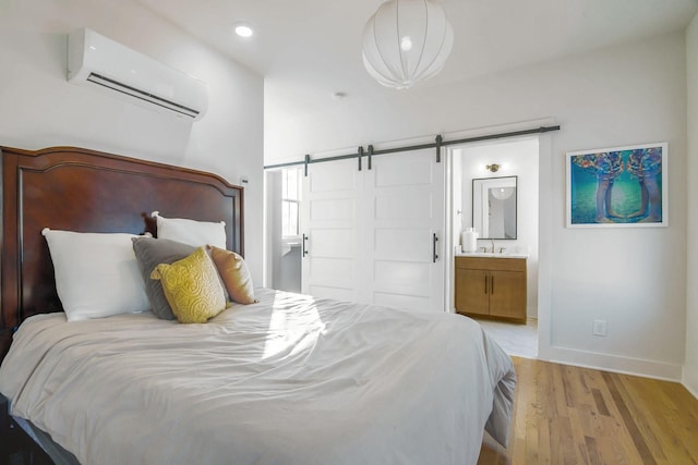 bedroom with ensuite bath, a wall mounted AC, light hardwood / wood-style flooring, a barn door, and sink