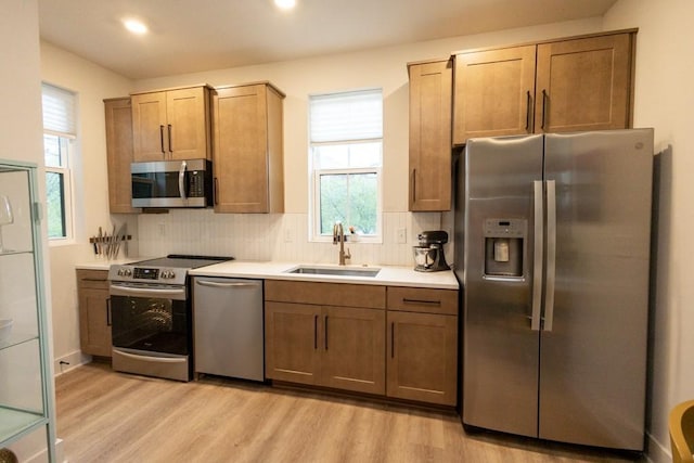 kitchen featuring appliances with stainless steel finishes, a healthy amount of sunlight, sink, light hardwood / wood-style flooring, and tasteful backsplash