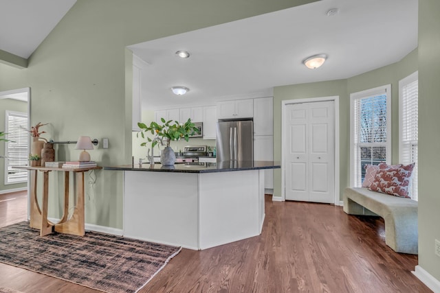 kitchen with stainless steel appliances, white cabinetry, kitchen peninsula, dark stone counters, and dark hardwood / wood-style floors