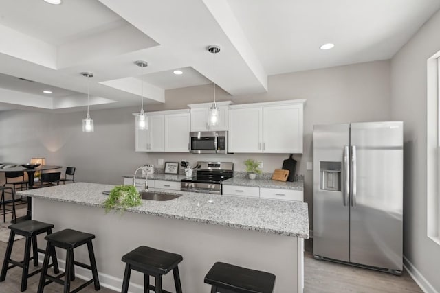 kitchen with a raised ceiling, a kitchen bar, white cabinets, appliances with stainless steel finishes, and sink