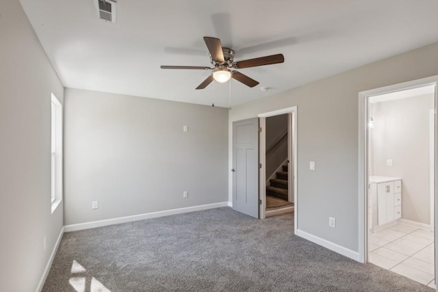 unfurnished bedroom with a walk in closet, ensuite bath, light carpet, and ceiling fan