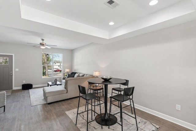 dining area with a raised ceiling, ceiling fan, and dark wood-type flooring