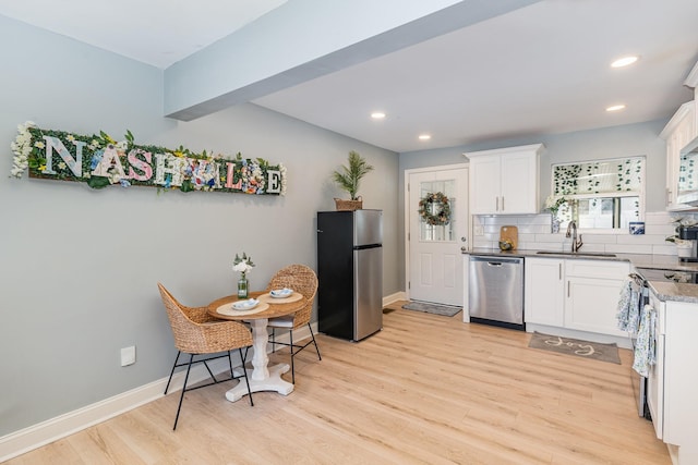 kitchen with white cabinetry, stainless steel appliances, decorative backsplash, light wood-type flooring, and sink