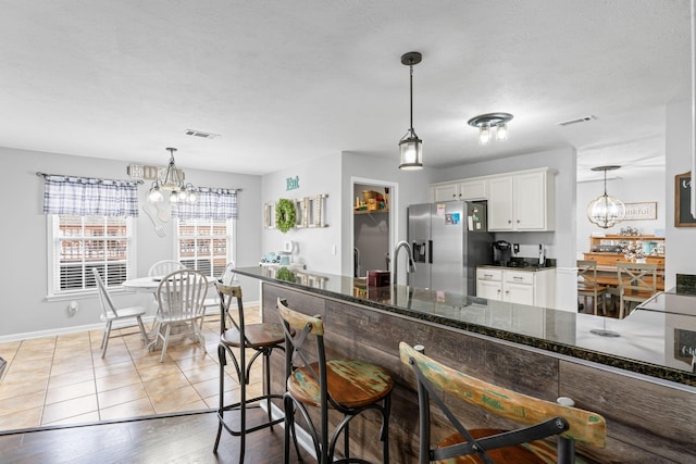 kitchen with white cabinetry, light hardwood / wood-style flooring, stainless steel fridge, and decorative light fixtures