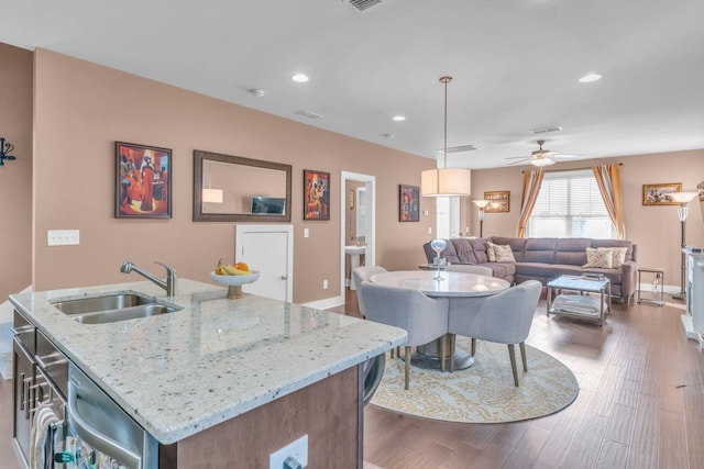 kitchen featuring an island with sink, light stone counters, dark hardwood / wood-style floors, sink, and decorative light fixtures