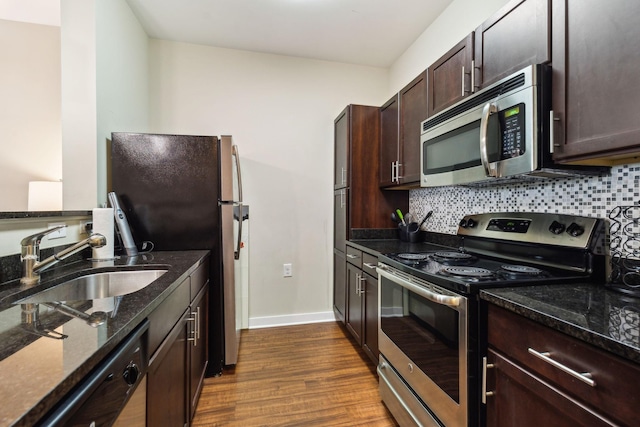 kitchen with dark wood-type flooring, a sink, appliances with stainless steel finishes, backsplash, and dark stone counters