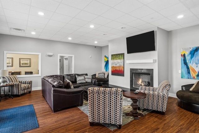 living area featuring visible vents, a lit fireplace, baseboards, and wood finished floors