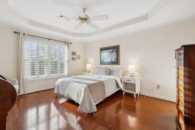 bedroom with wood-type flooring, ceiling fan, and a tray ceiling